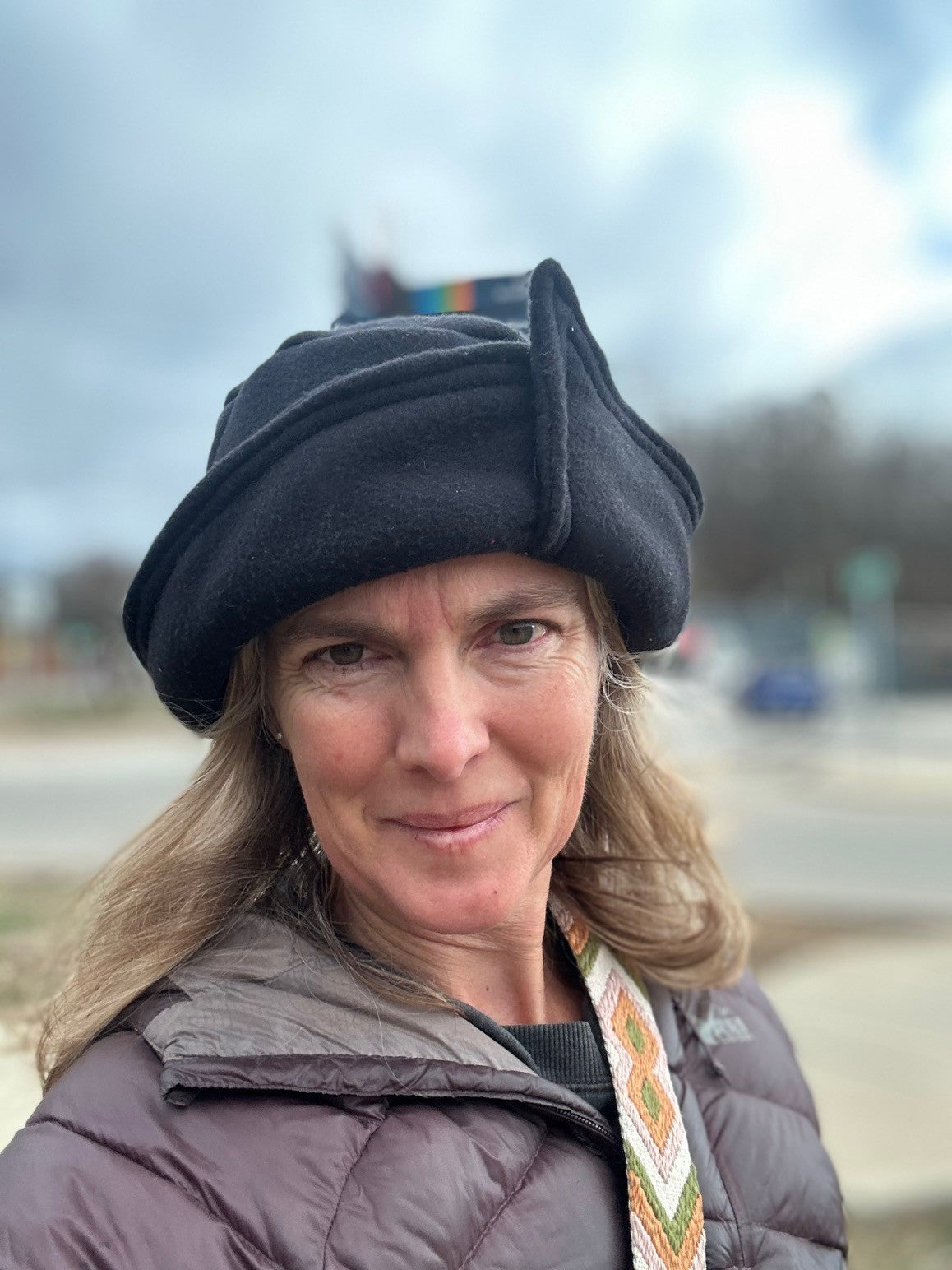 Woman wearing a black roll brim hat outside. Hat has an overlap with corner on brim.