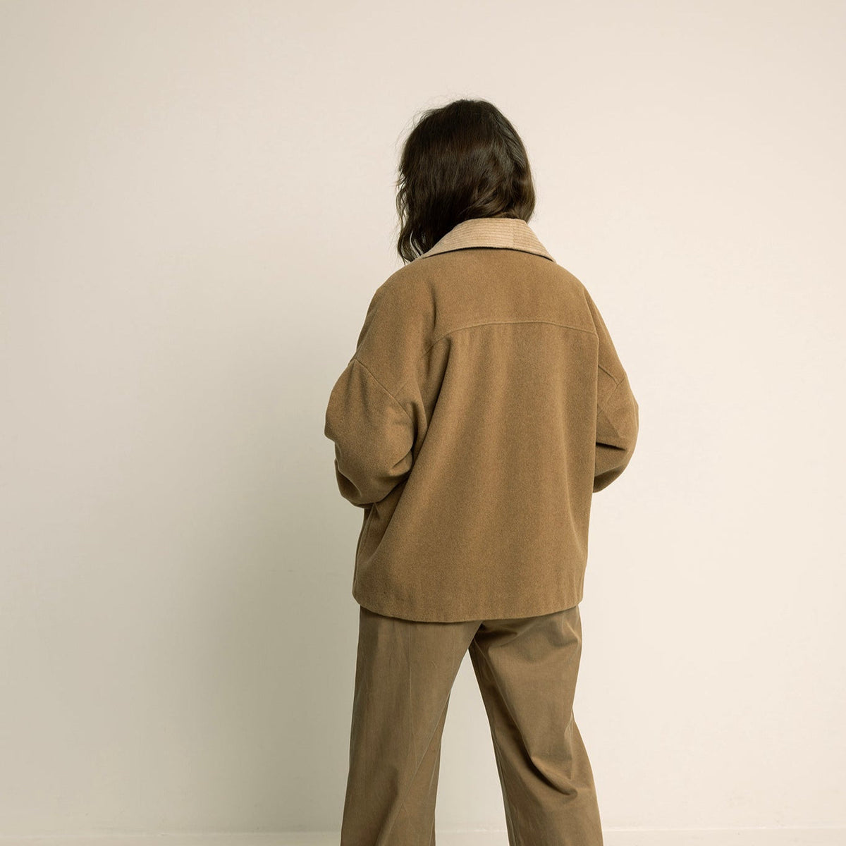 Person wearing a beige suit standing against a plain background