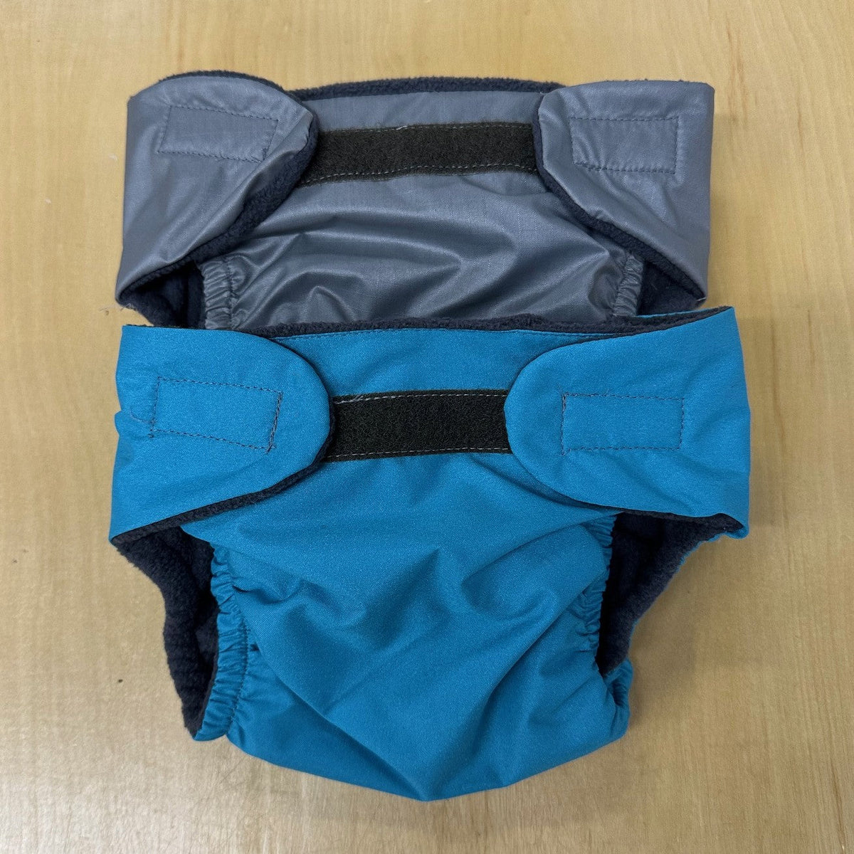 Blue and grey baby diapers with black velcro on a wooden surface