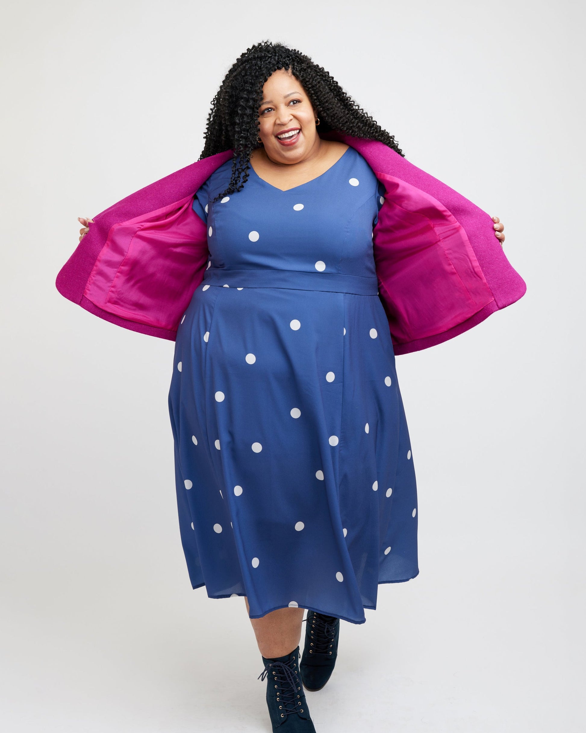 Woman wearing a blue dress with white polka dots and a pink jacket on a white background. This blazer is the Auburn Blazer sewing pattern from Cashmerette.