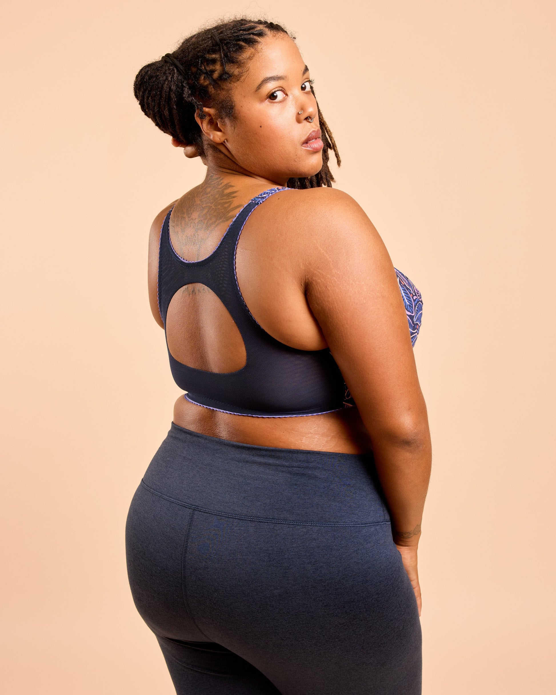 Woman wearing a black sports bra and leggings on a beige background. This is the Cashmerette Somerville Sports Bra sewing pattern for big boobs.