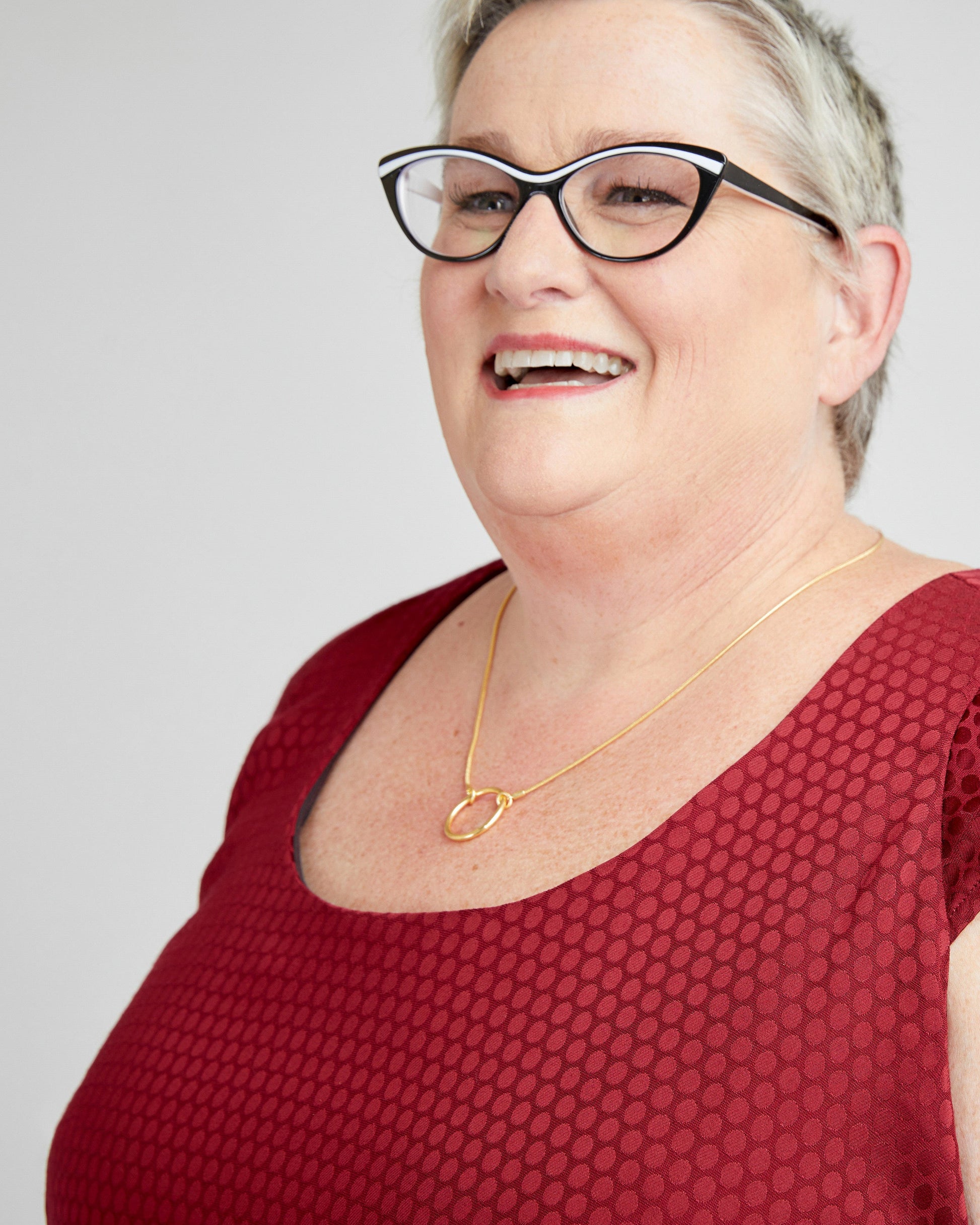 Woman wearing glasses and a red top with a gold necklace on a white background. This dress is the Upton Dress & Skirt sewing pattern from Cashmerette.